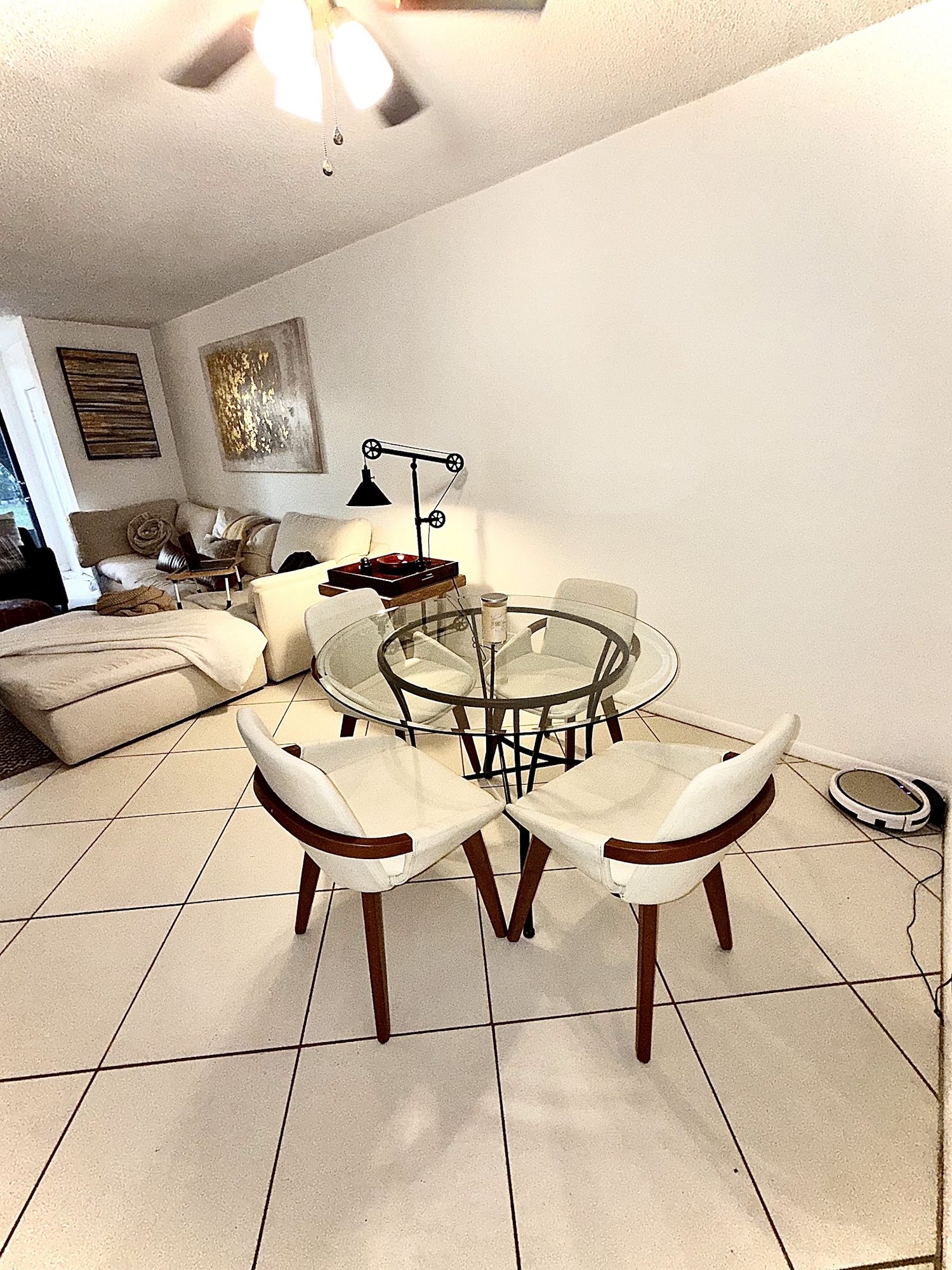 Dining area with glass table and four chairs beside bright tile flooring